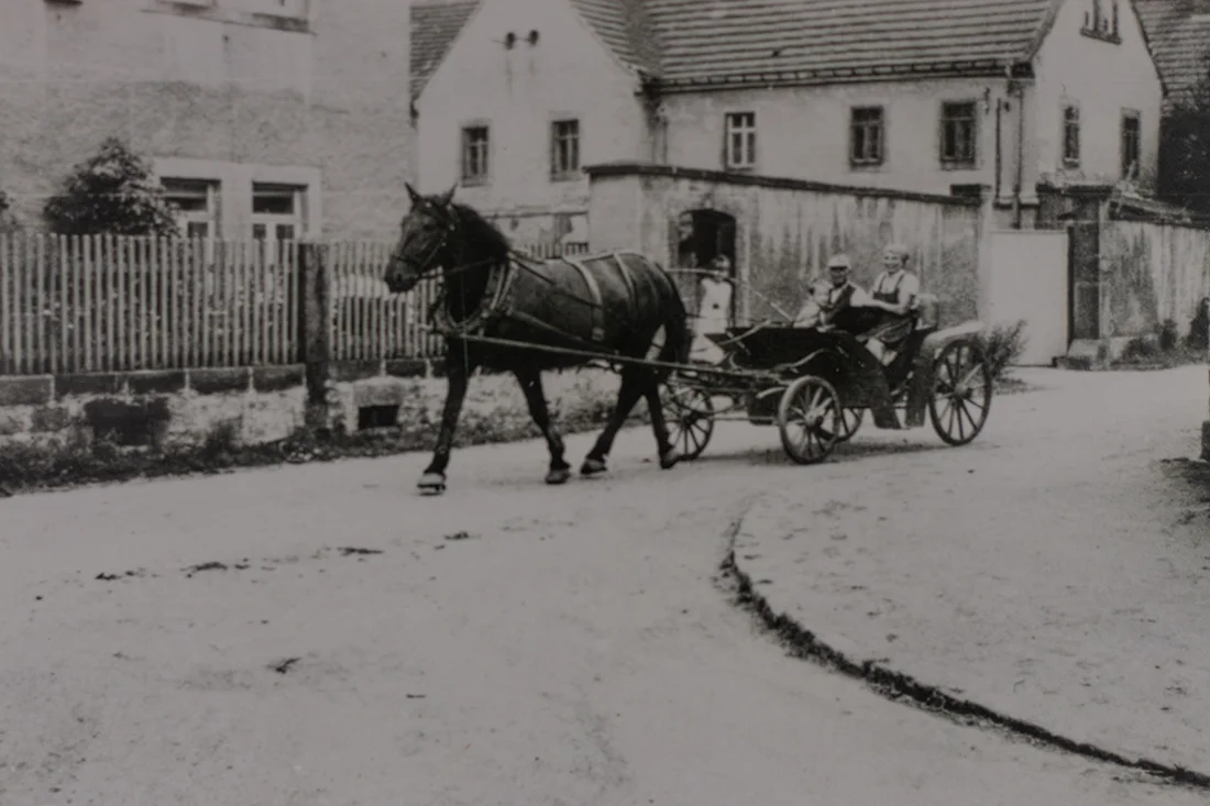 Hofansicht aus dem Jahr 1960. Ein Pferdefuhrwerk mit einem Paar fährt vor dem alten Hofgebäude in Gohlis vorbei.